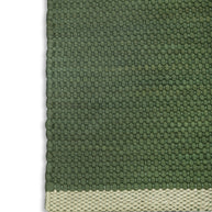 Close-up of a green textured rug with a beige border highlighting the corner detail